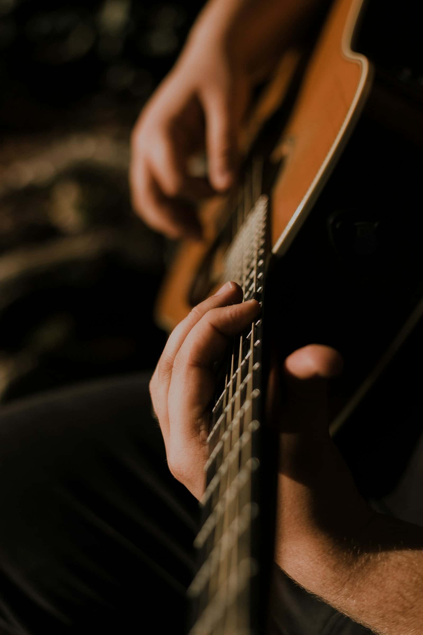 Hands on the neck of a guitar in low light