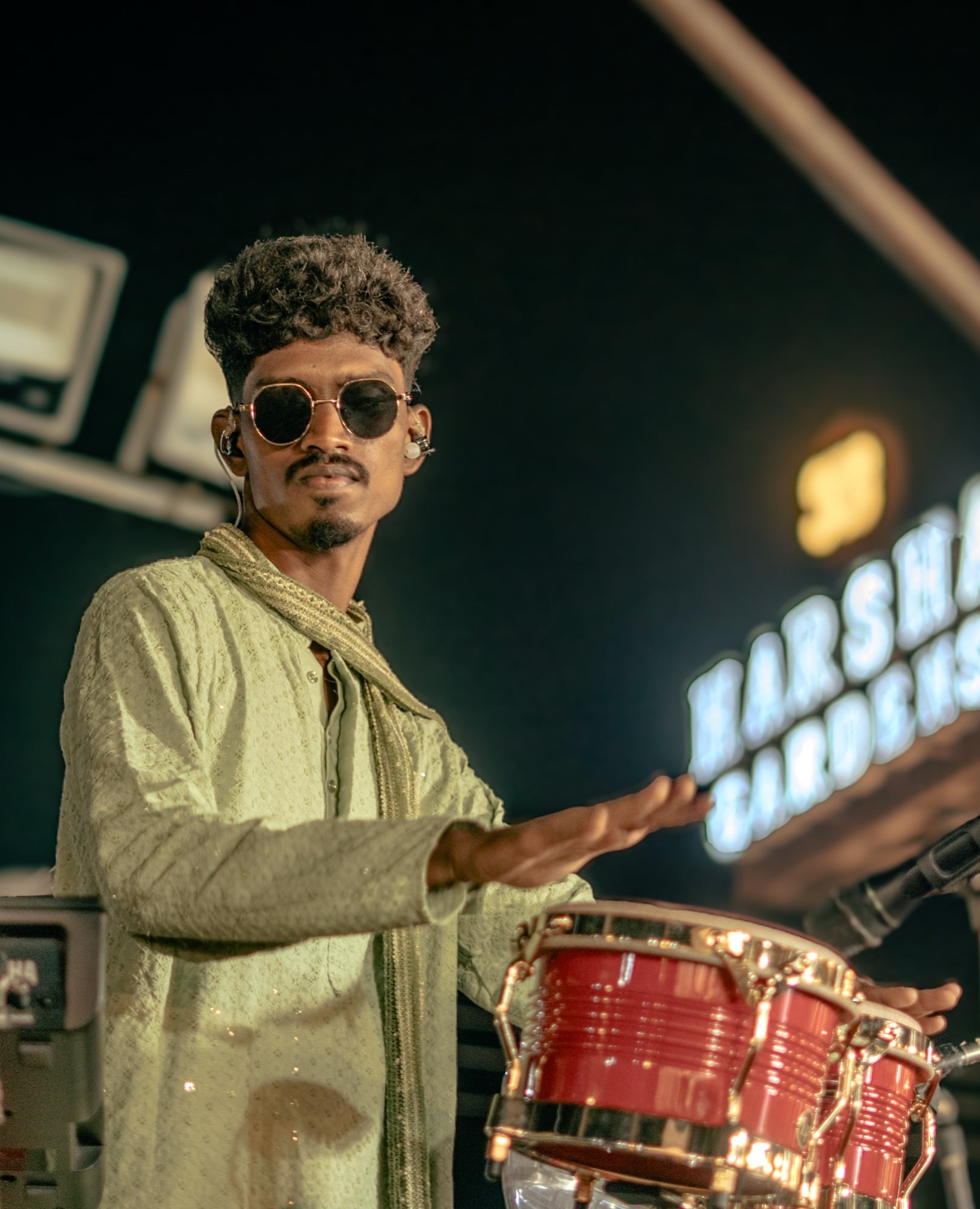 Jason in sunglasses and a pale-green kurta playing red bongos on stage